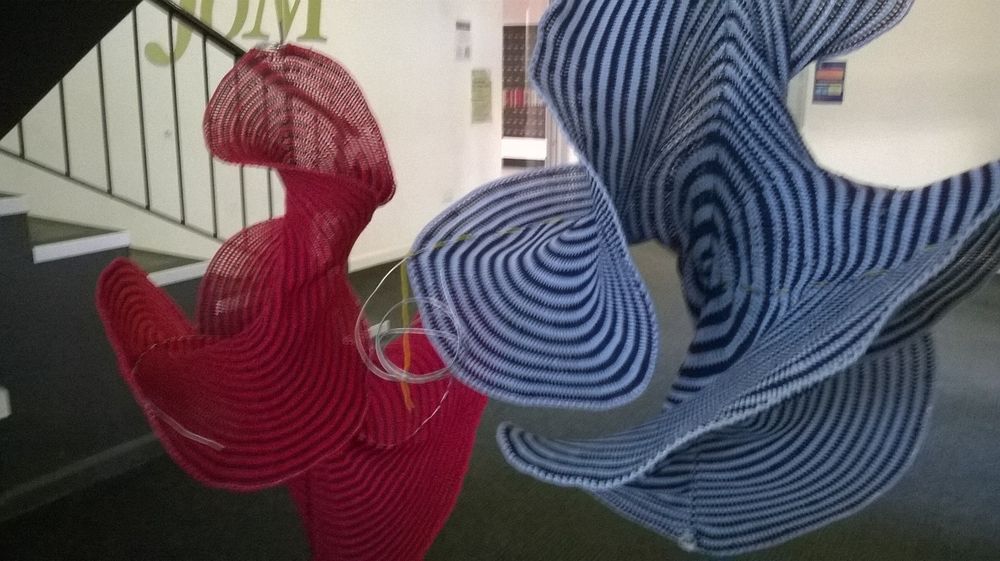 Red and blue crocheted surfaces that have wires around their edges. They are lopsided and sagging.