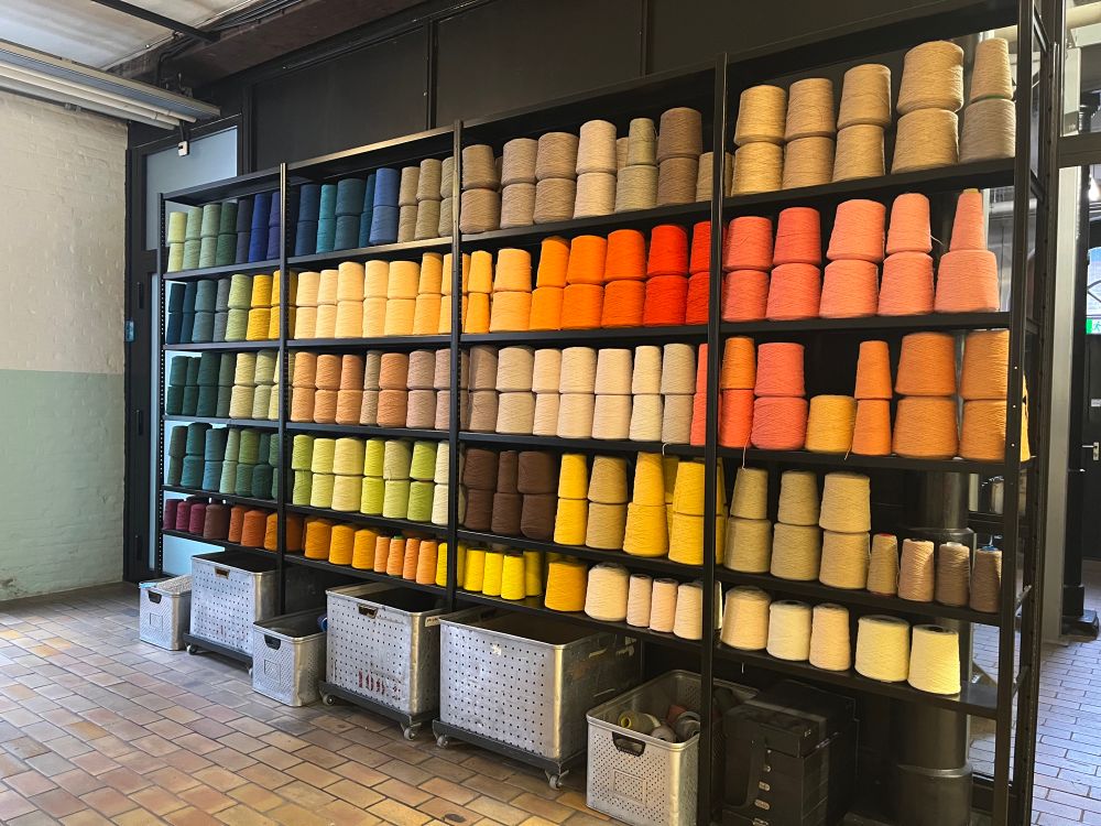 Shelves containing cones of yarn in a spectrum of colours. 