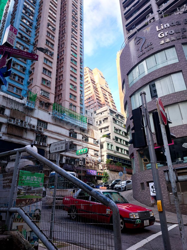 香港の街並み。高くカラフルなマンション群、坂道、オレンジ色のタクシー。