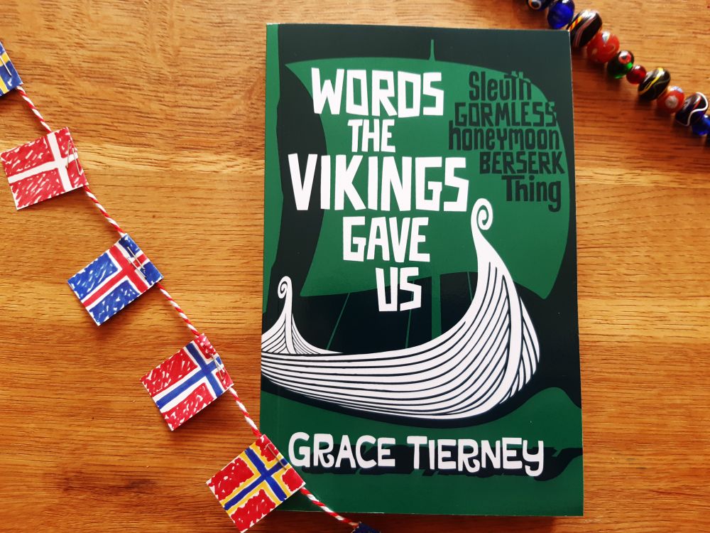 Words the Vikings Gave Us by Grace Tierney in green and white cover with longship motif, draped with Viking beads and tiny Viking country flags