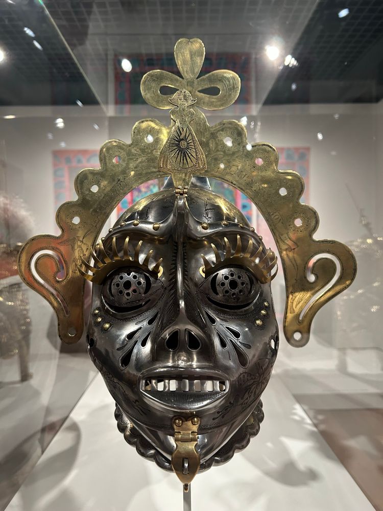 A commission by Grayson Perry to have one of his ceramic masks made into a knights helmet. The result is a brushed grey mental face with golden eyelashes, ears and stylised crown. Entitled something like the sissy’s bridle