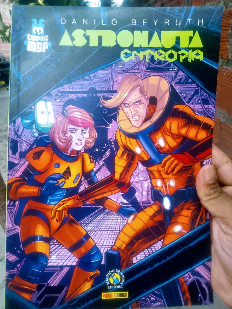 Capa de Astronauta Entropia publicado pela Editora Panini. A imagem traz o protagonista, Isa e um robô em forma de cachorro. Atrás a silhueta de um alienígena observando-os. 