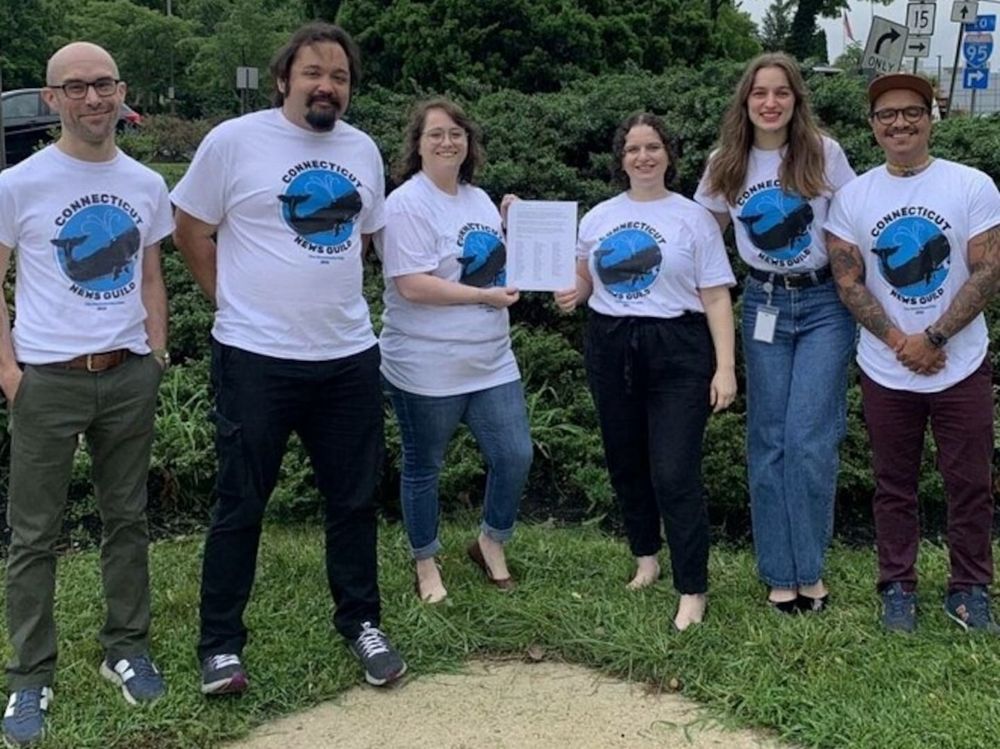 Six smiling Hearst CT employees wearing beautiful whale t-shirts hold up a mission statement signed by dozens of members 