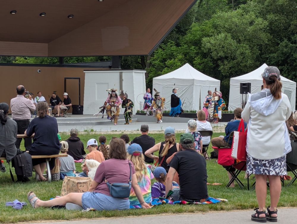 People sitting in front of a stage where powwow dancers in regalia perform the Grand Entry.