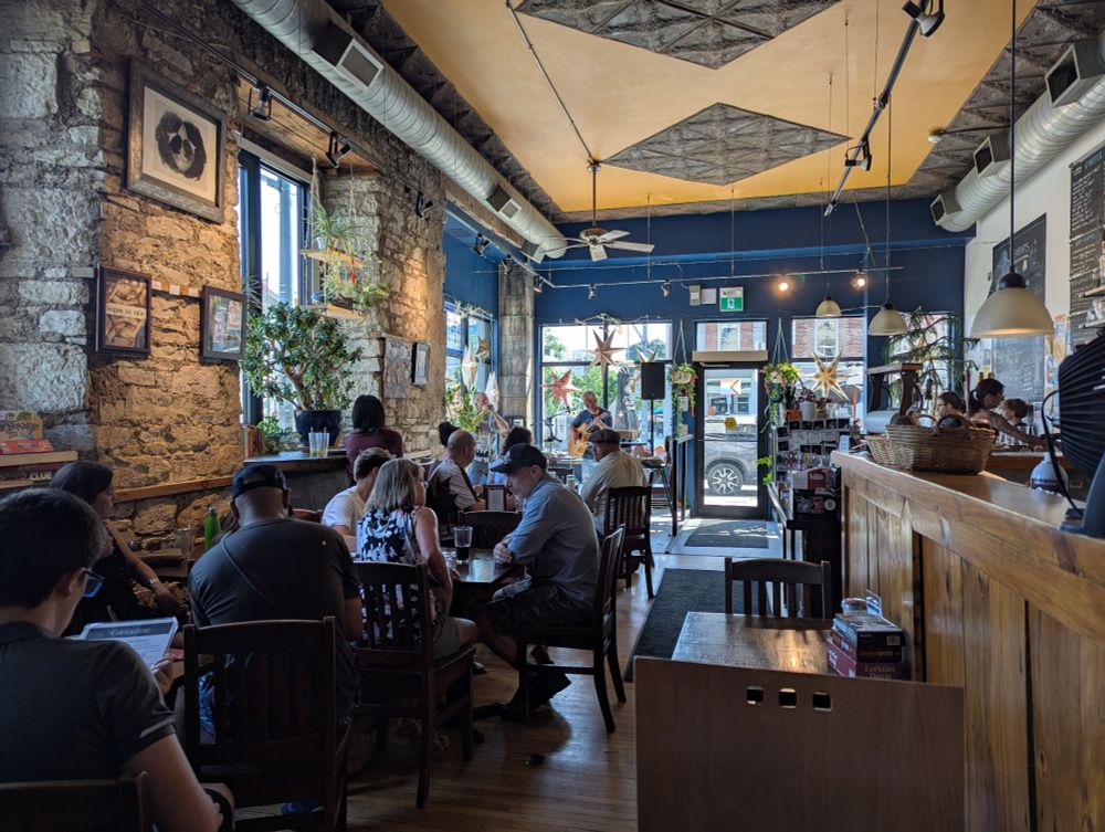 A café with tables filled with people. In the back close to the entrance is a small stage with two musical performers.