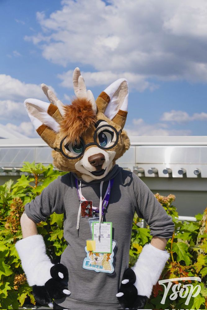 The owner of this account wearing a deer dragon partial fursuit, posing in front of some greenery