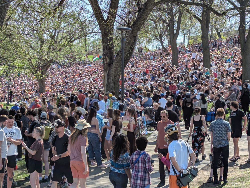 A huge crowd of people enjoy beautiful weather in a wonderful city park.