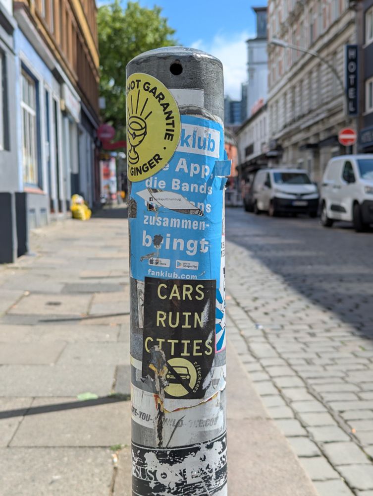 A bollard covered with stickers, including one that says cars ruin cities.