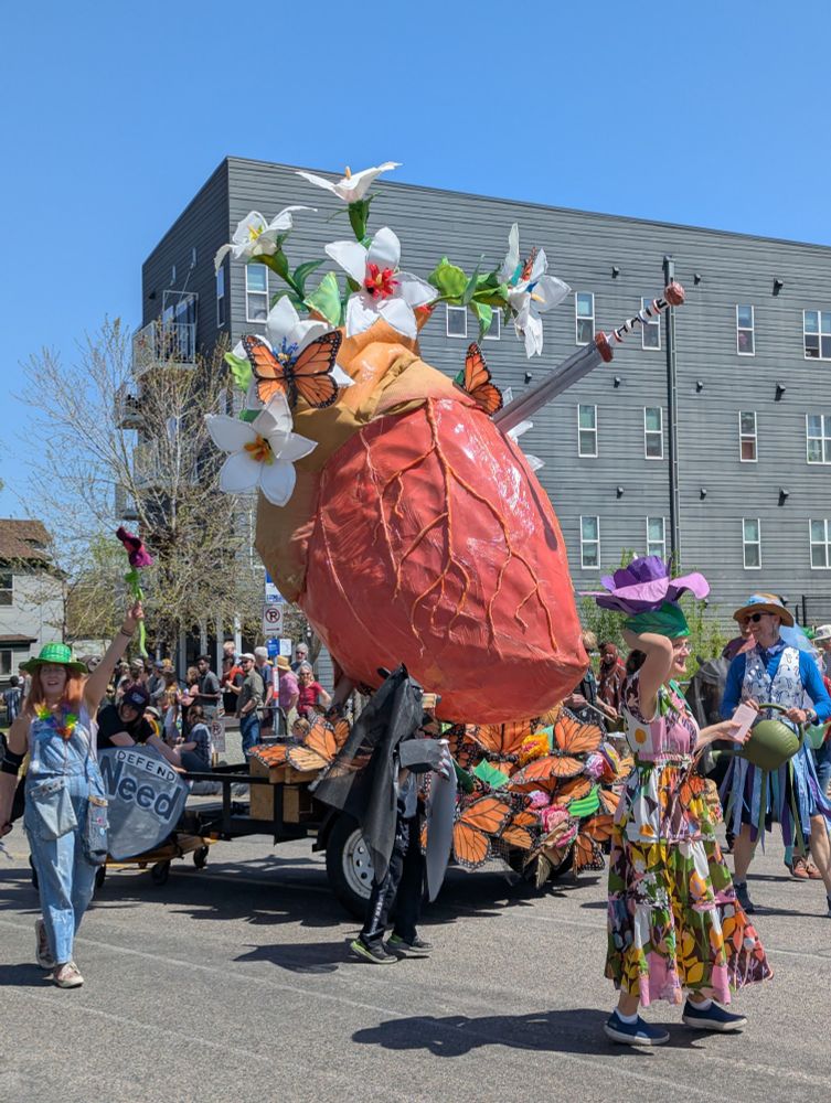 A giant heart with flowers growing out of it and costumed people walking around 