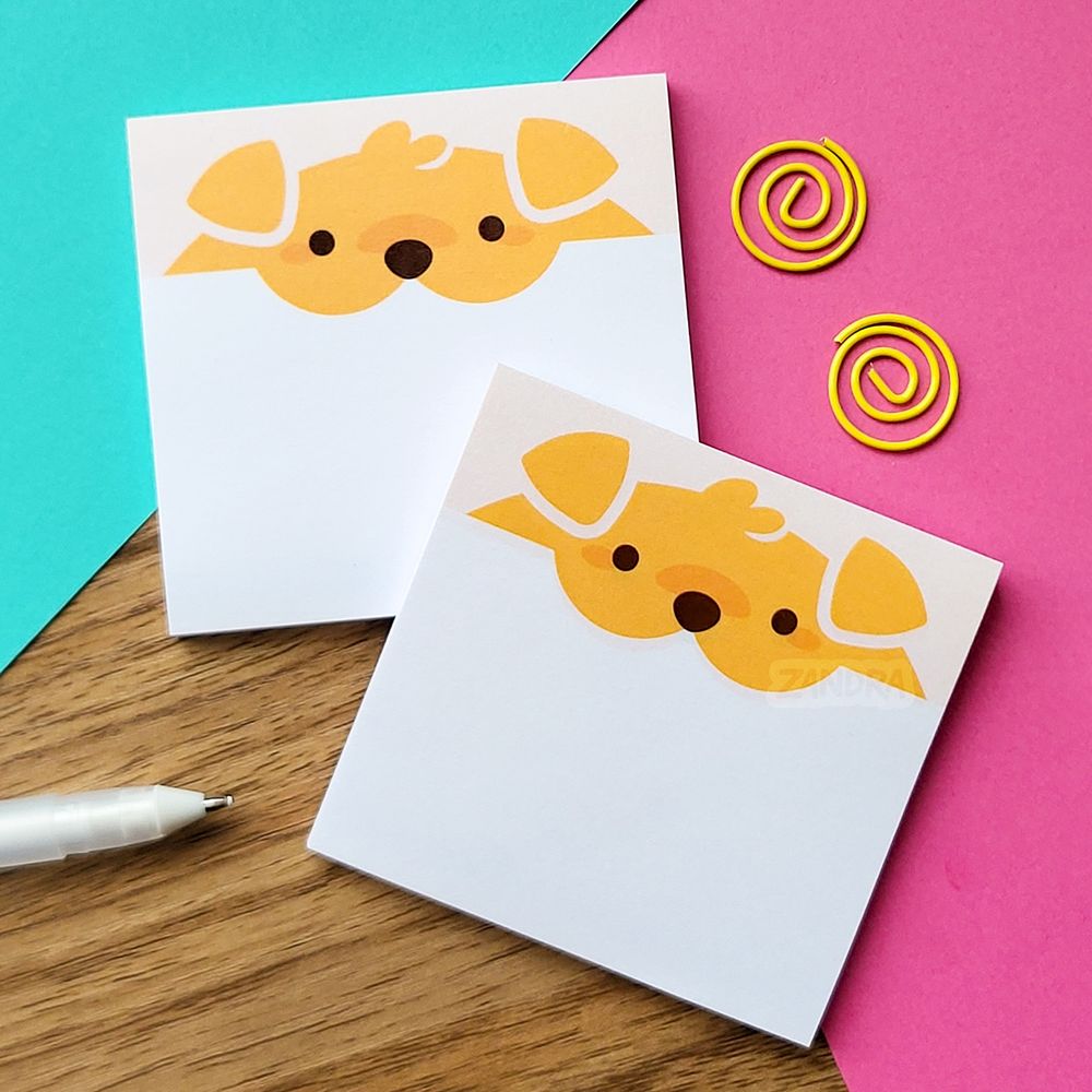 a photo of two sticky note pads on a colorful paper background. the sticky note design features the head of a golden retriever dog chomping on the top of the sticky note.