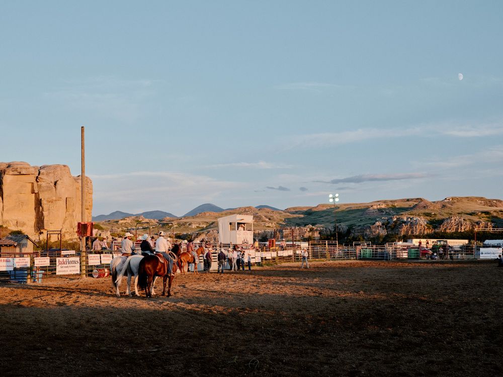 Rodeo at Writing-on-Stone Provincial Park, Alberta.

A golden-hour rodeo scene set against the sandstone hoodoos and rugged hills of Writing-on-Stone Provincial Park. Cowboys on horseback gather in the dusty arena, with spectators and fencing in the background. The light is warm and cinematic, with long shadows and a visible moon overhead.