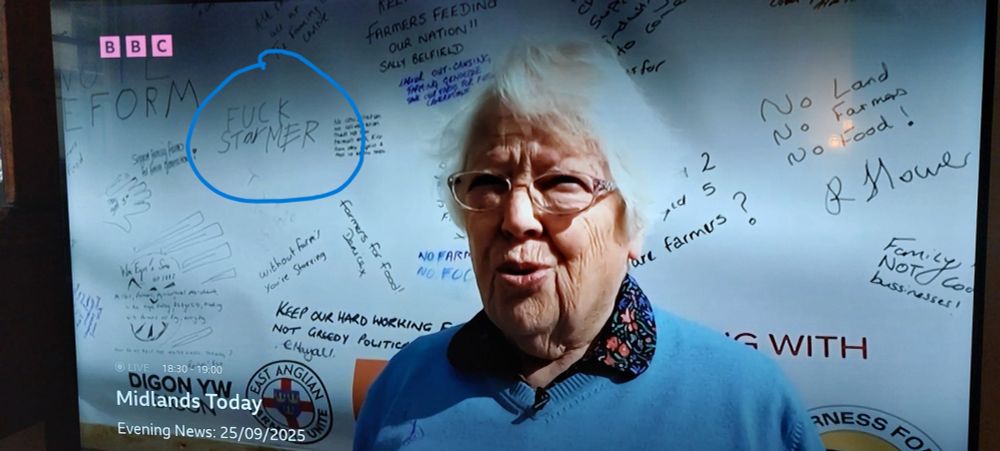 A screenshot of a lady being interviewed on BBC MIdlands Today against a backdrop with handwritten messages from angry farmers, including one just next to her head that says "Fuck Starmer"