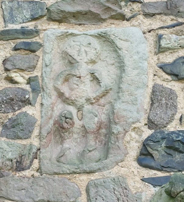 Close up of an anciant Sheela Na Gig on the wall of a church in Shropshire. She is a crudely carved figure of a woman with her legs open 