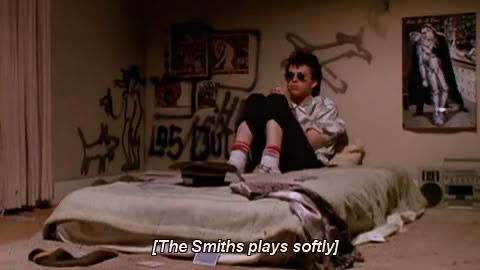 Ducky sits listening to the smiths in bed, fully dressed, including with his sunglasses and sneakers 