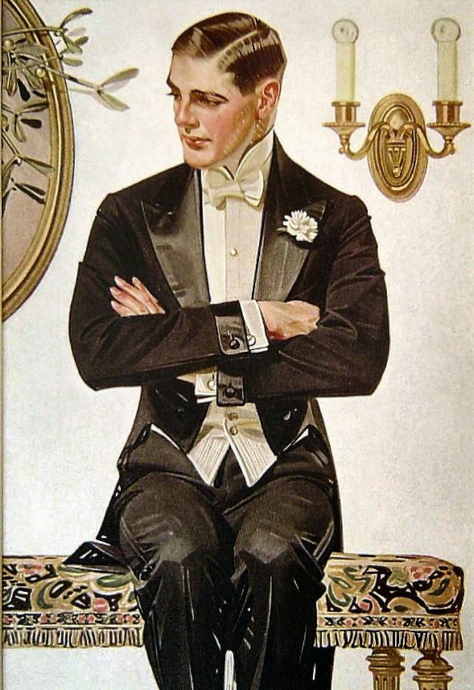 An Andrew Loomis painting of a young man in his twenties in a black dinner suit with a white flower in the lapel, a white buttoned shirt and a white bow tie. He sits on a table covered with an intricate cloth with what looks like a gold candle stick holder with two long candle-like lights with electric bulbs on top on the wall on one side behind him and a oval shaped piece of wall art partially in panel on the other side. He looks away from their viewer and to the left, head slightly tilted down.
