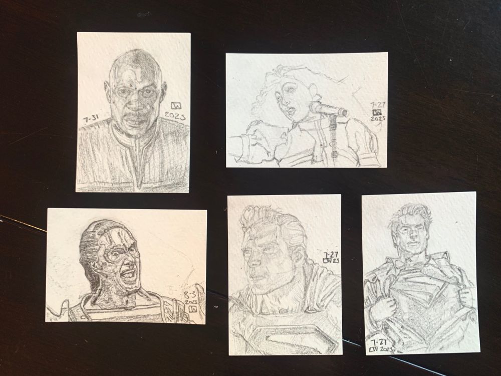 Five paper sketch cards sit on a wooden surface, each with a portrait drawn in pencil. 

From right to left: one of the top two is Captain Sisko from a front view, his face partially in shadow, drawn 7-31 LW. Next to that turned in landscape view is a bust portrait of Chapelle Roan in front of a microphone in a puffy-sleeved dress looking away from the viewer towards the left. Her card has the least amount of detail and is not shaded in. Drawn 7-27 2025.

The three cards on the bottom row consists of Garak from Deep Space Nine, looking exited and happy in a striped shit with an open vest with jazz hands only partially visible drawn 8-3 2025 and then we have two sketch card portraits of Superman from the new movie, one is a front view of him pulling back a button-up shirt to reveal the Superman logo and the other card is a closer 3/4 view of him looking off to the left in his full uniform, both drawn 7-27 2025 LW.