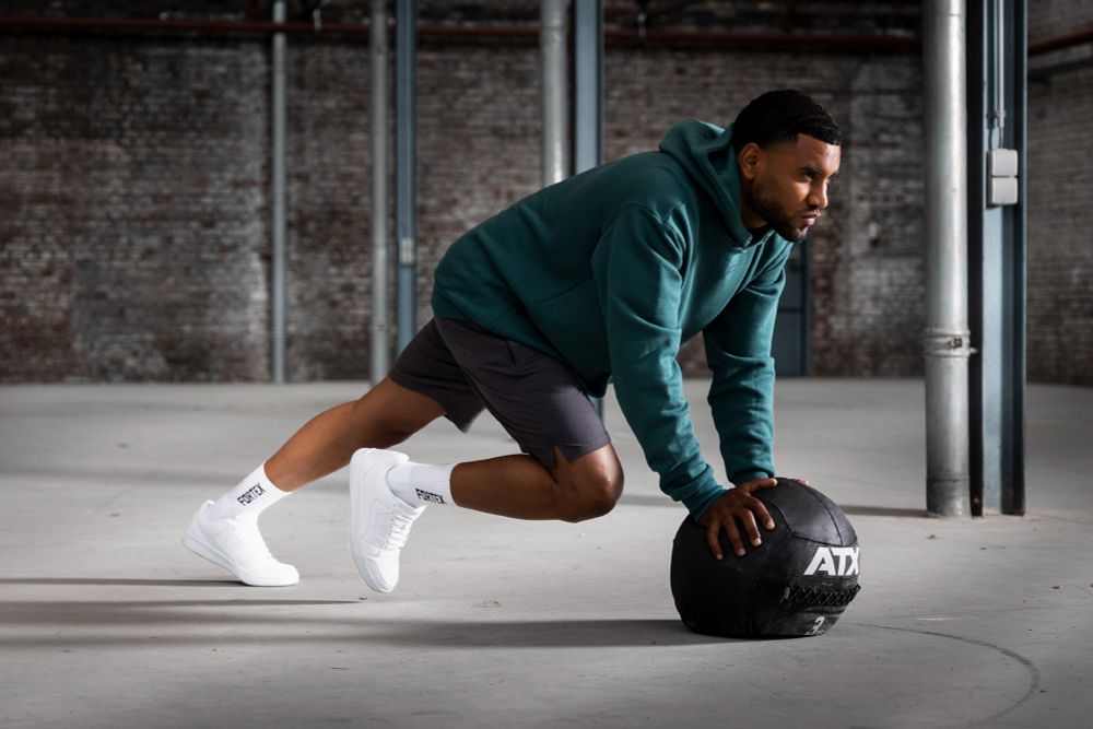 A guy in Fortex Fitness apparel, doing an exercise with an ATX weight ball. He is doing his workout in a large industrial space with steel beams and lots of concrete.