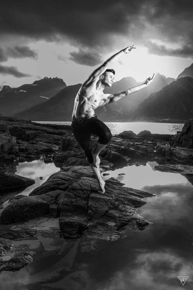 A male ballet dancer standing in the wilderness. He has a long stretched pose while it looks like he grabs the sun between his hands