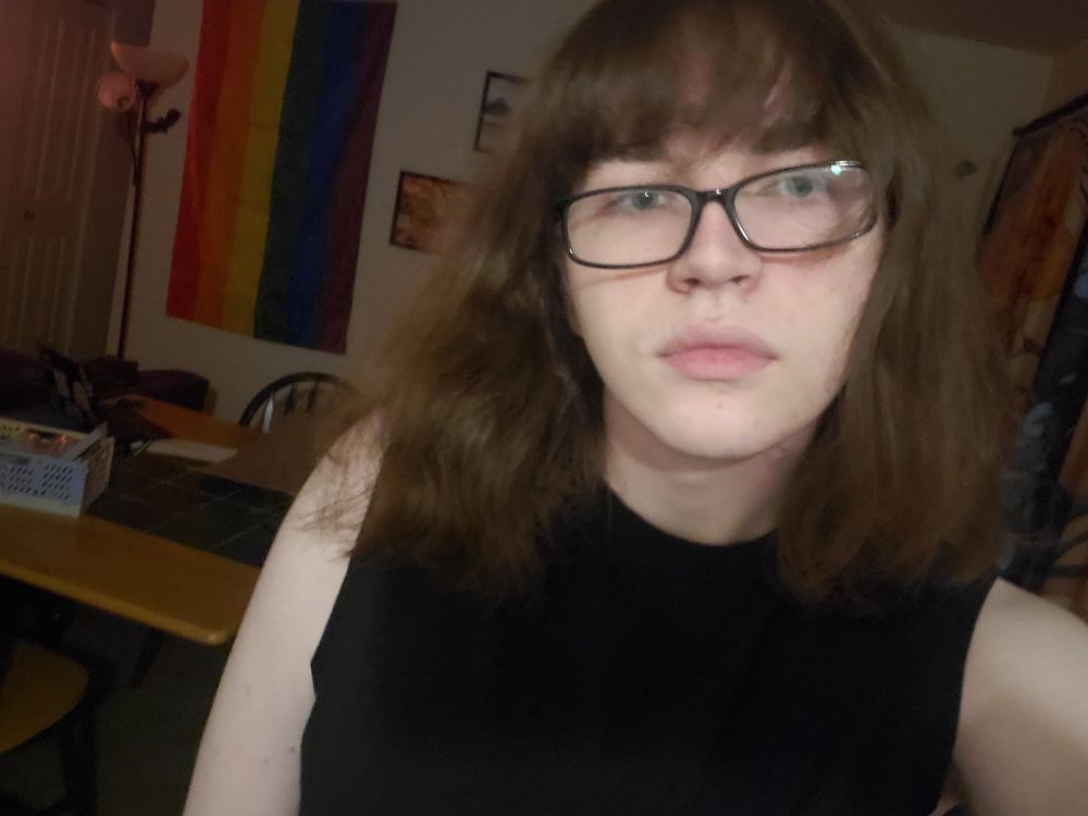 A selfie of me in a sleeveless shirt, i have bangs reaching my eyebrows and the rest of my hair is shoulder length