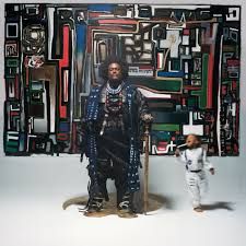 Photo de Kamasi Washington tenant un katana, dos à un mur peint comme un tableau d'art abstrait. Sa fille court en flou de mouvement à côté de lui