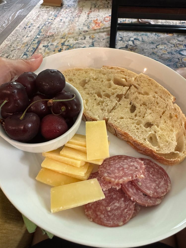 A plate of cherries, cheese, salami, and two half slices of sourdough bread with butter