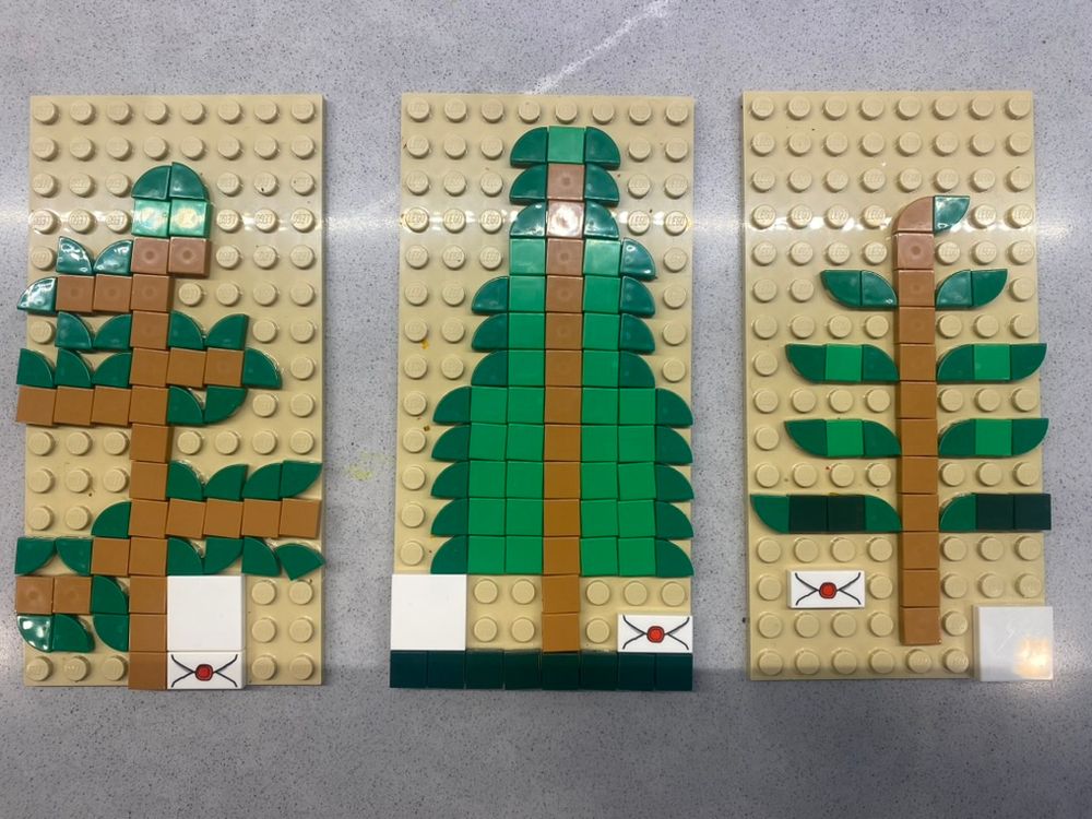 three small lego plates decorated with a single layer of brown and green flat, square legos that create three pixelated pictures of an herbarium specimen, complete with label (blank white 2x2 square) and envelope packet (1x2 piece with envelope styling).