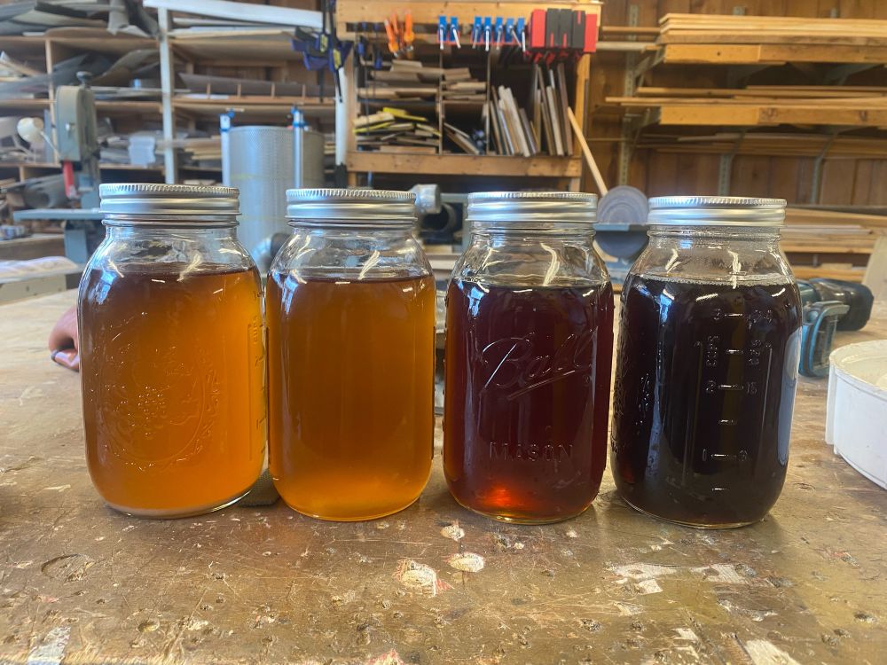 a row of 4 mason jars full of maple syrup — the syrup ranges from a light golden amber to a deep rich coffee brown.