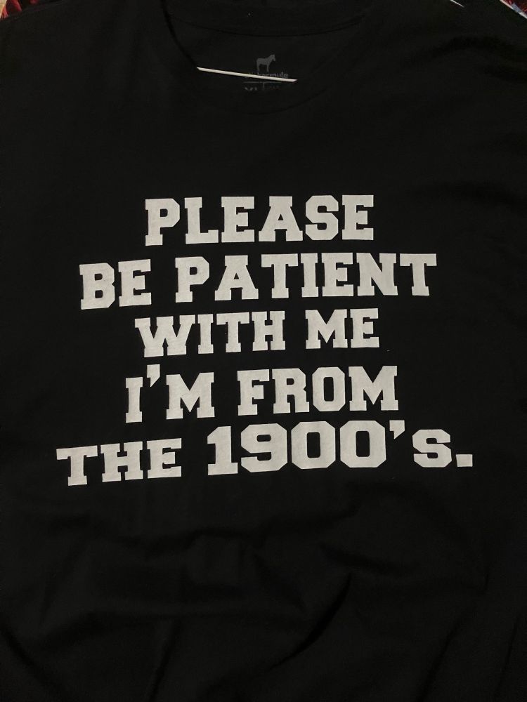 A black shirt with white printing that states. Please Be Patient With Me I’m From The 1900’s.