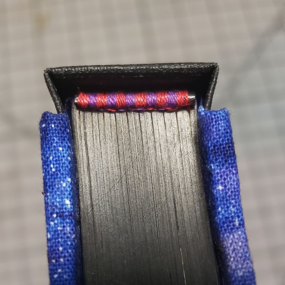 Close up of endbands. They are made from red and purple embroidery floss over a black pleather cord.