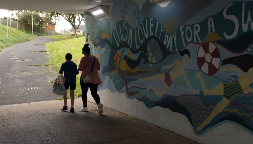 Photo of people walking through underpass with graffiti art on wall 