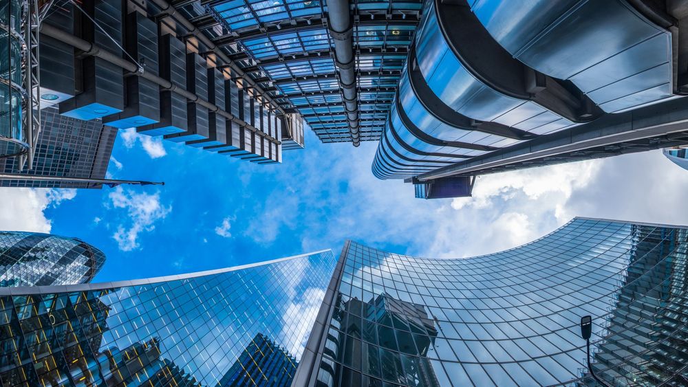 Looking up at modern skyscrapers with reflective glass and metal surfaces against a blue sky with clouds.