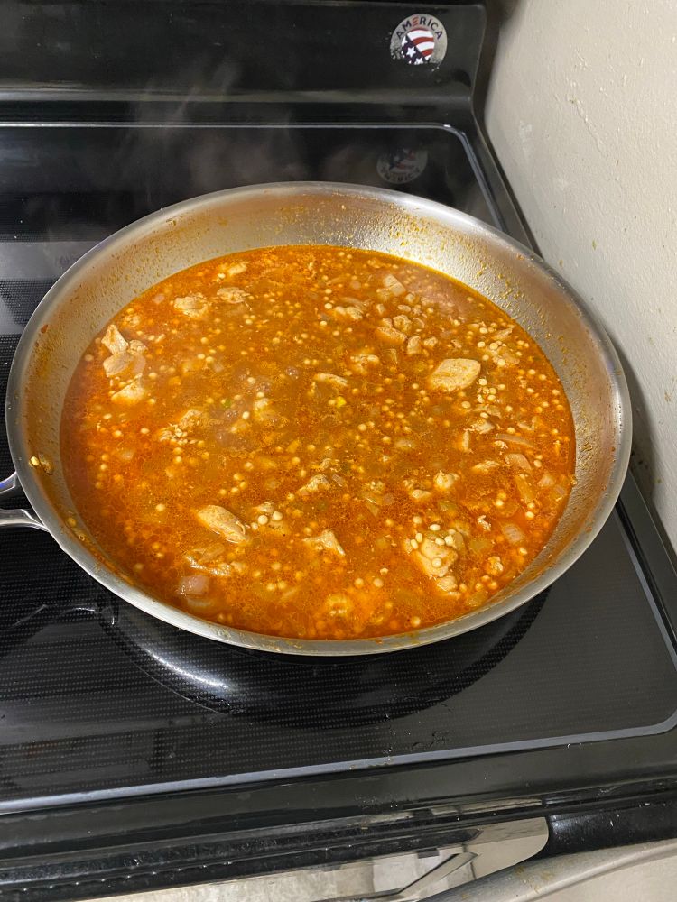 chicken thighs & couscous cooking together in a paprika sauce on the stove