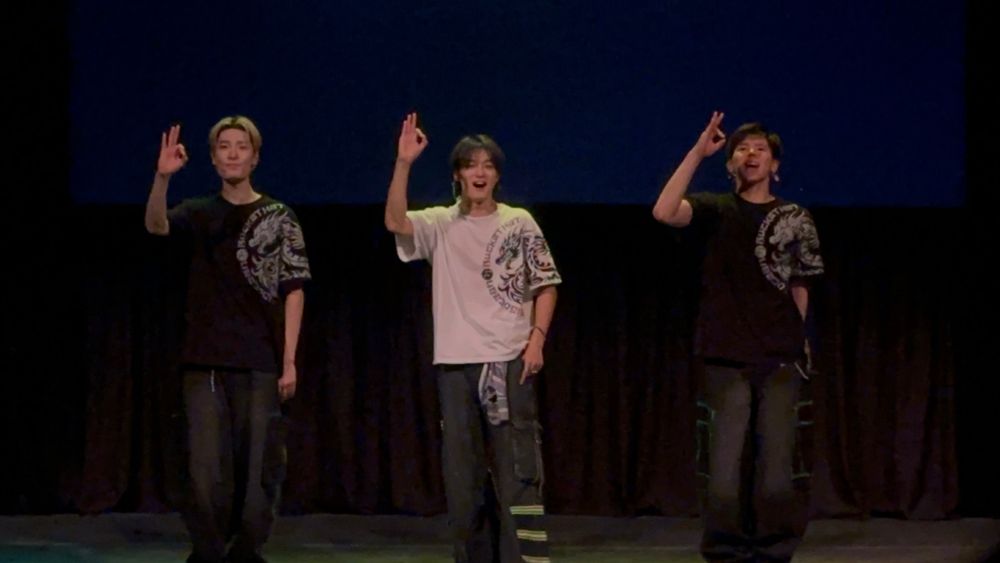 Big Ocean on stage doing the Big Ocean hand Sign they are in order from left to right Jiseok, Pj, then Chanyeon. They are all in jeans. Jiseok and Chanyeon are both in Black Bucket hat Shirts and Pj is in a White Bucket Hat shirt.