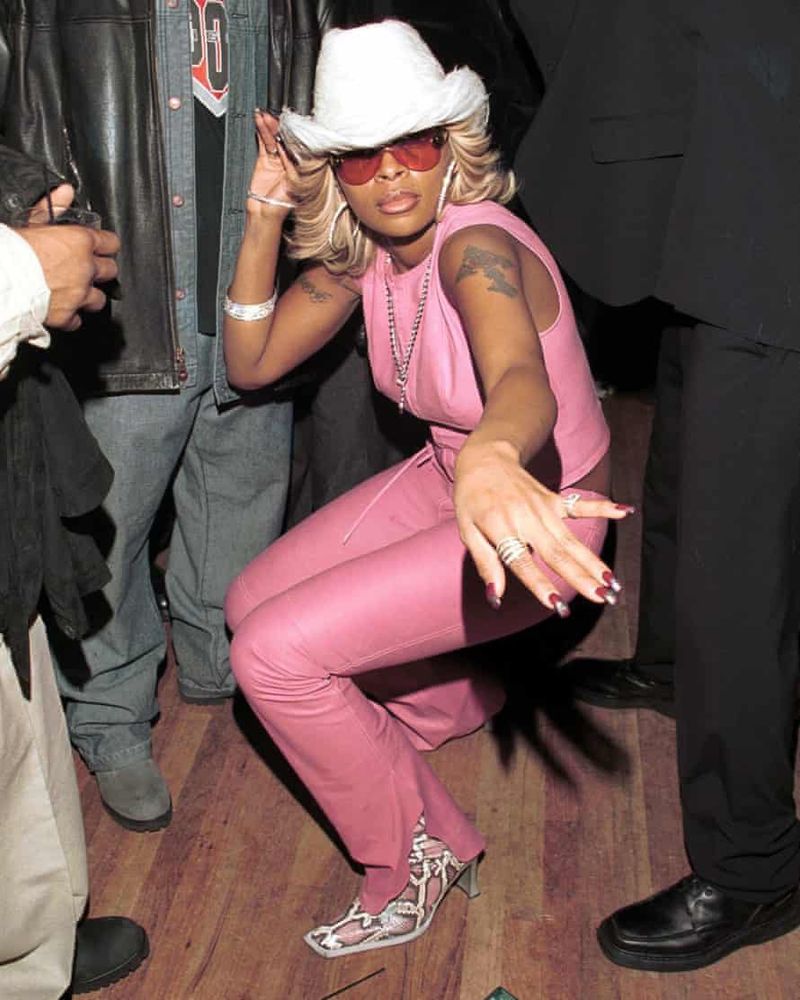 Mary J. Blige wearing a pink leather crop tank pant set with a white cowboy hat, white snakeskin boots, pink sunglasses & platinum jewelry.

She is captured in a crouched position seemingly in transition to her next dance move. 