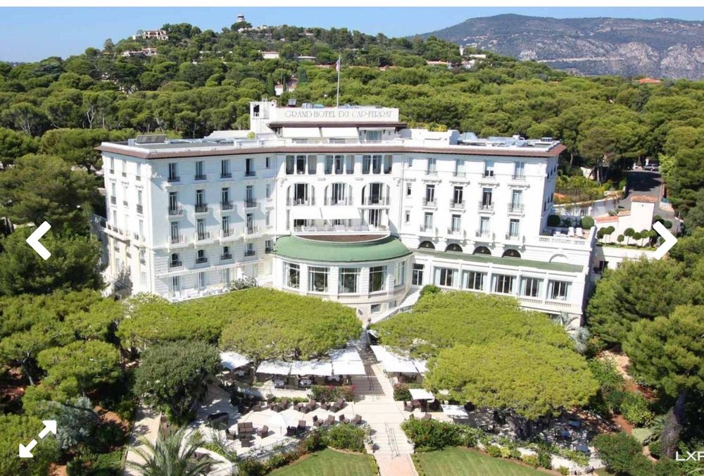 Grand-Hôtel du Cap-Ferrat which is a large white stately-looking building sitting on a hill. There are trees in the front. 
