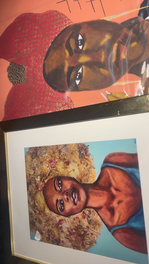 Two paintings next to each other horizontally. The bottom one is of a woman from her head down to her chest. She has an Afro made of flowers and a blue tank top. The top one is of just a woman’s face. Her hair is pulled back into a bun and she has a large red bow and earrings dangling down to her shoulders.