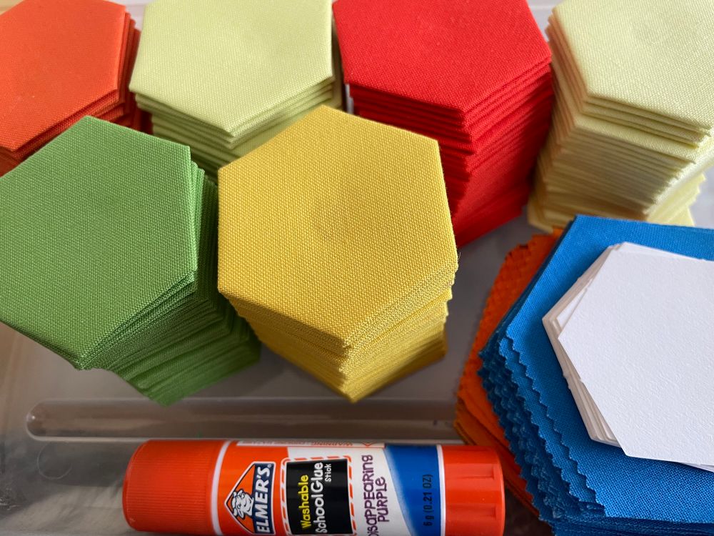 Hexagonal cotton fabric pieces in many colors, alongside a glue stick 