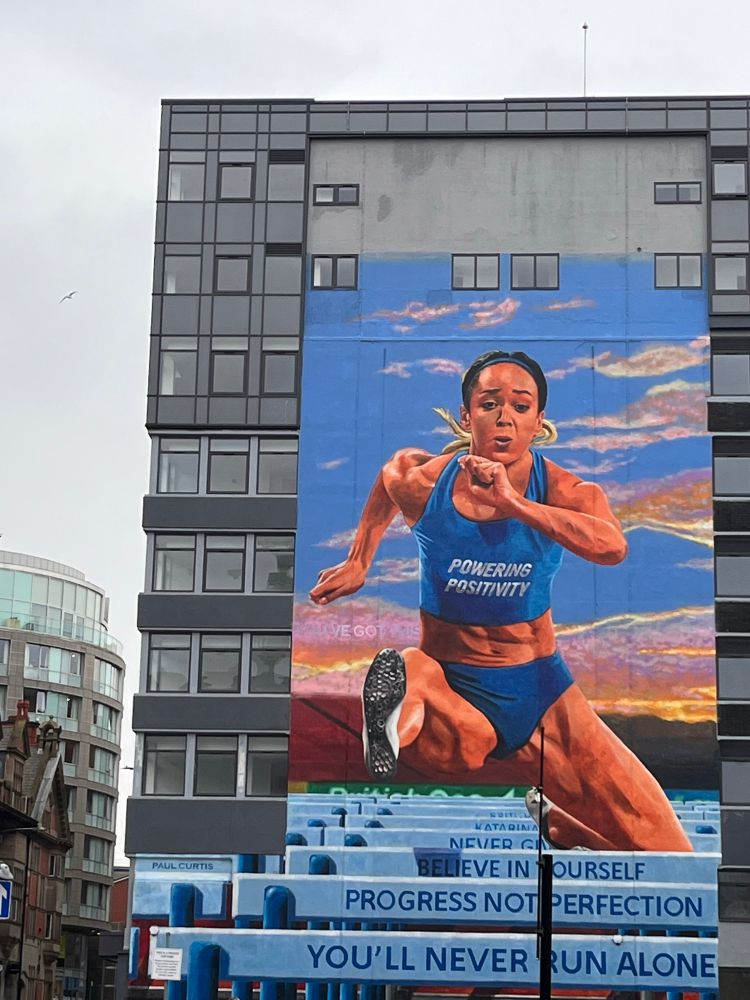 A large office building decorated with a huge mural of Katarina Johnson Thompson hurdling. 