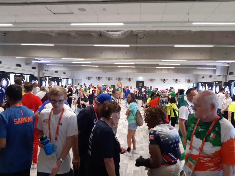 Ein großer Raum mit vielen Menschen, an den Wänden links und rechts stehen Dart-Scheiben.