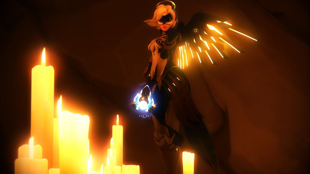 Overwatch 2 screenshot of Mercy in her Owl Guardian cosmetic - it is her typical flight suit but it is mostly in navy and gold detailing that looks French, with an owl mask on her face and yellow/gold accents on her wings. She is standing in a cave with soft diffused light from the candles at her feet, and she has her staff out. 