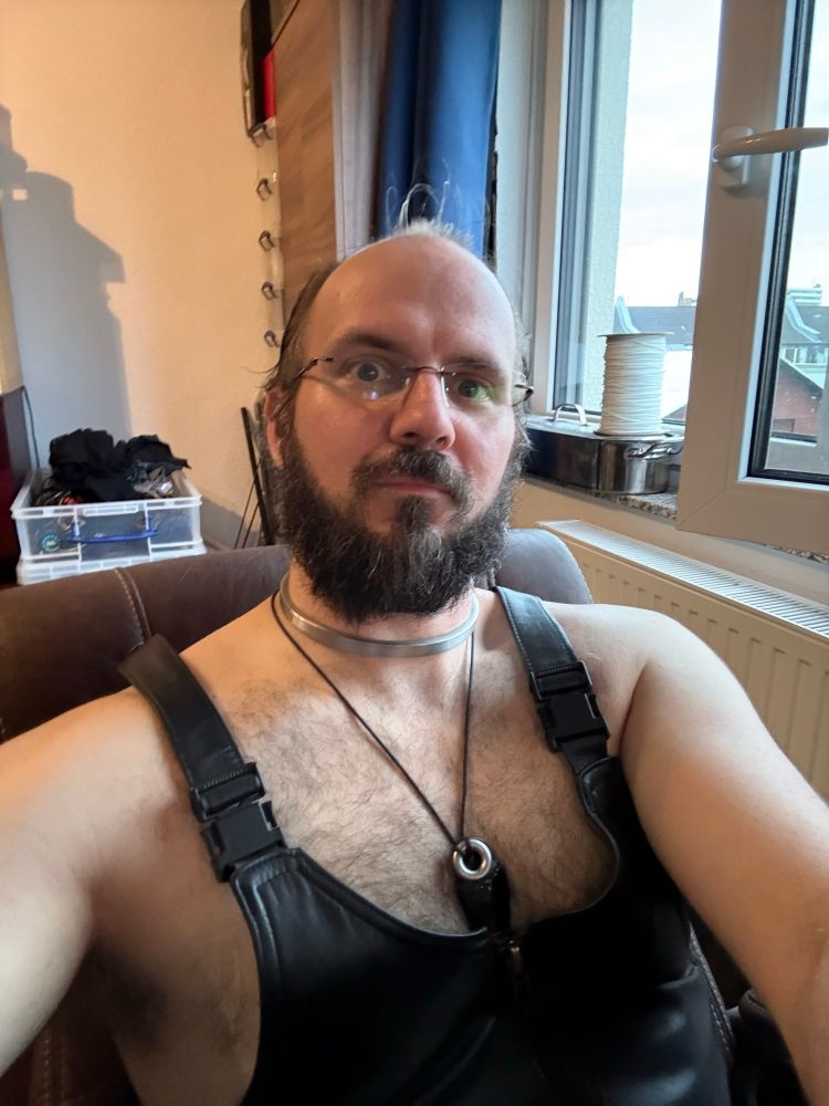 A picture of me sat in my computer chair relaxing on the evening, wearing my leather salopettes and my beard being rather long and bushy (and in need of a trim perhaps) 