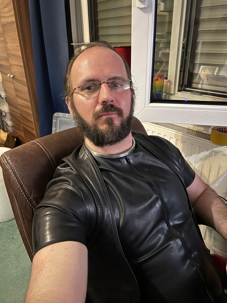 Me, sat in my computer chair while writing my memoirs. 
Wearing a rubber suit and leather waistcoat. Still wearing my new collar.