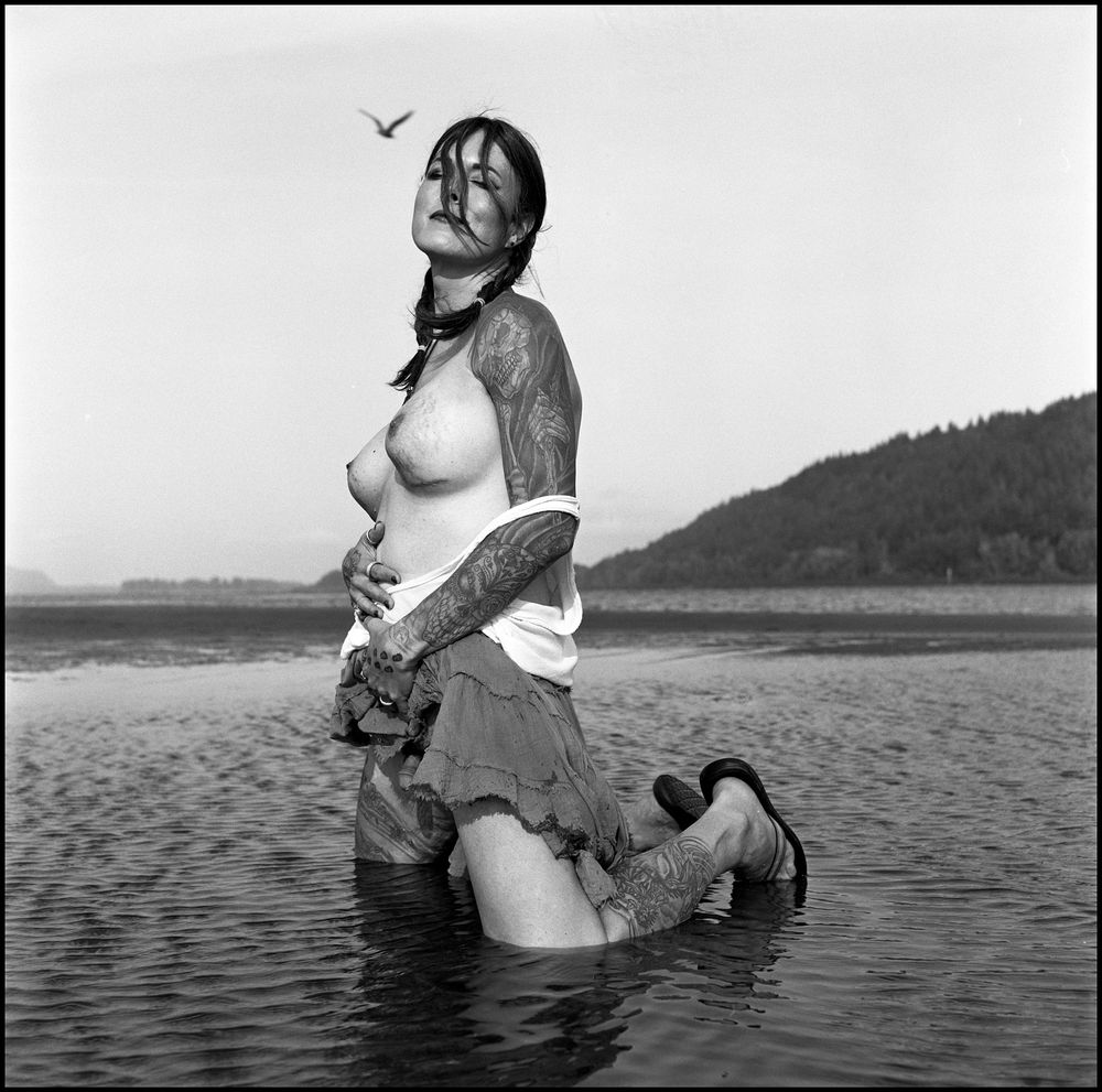 Jade kneeling in the water. Her head is tilted upwards and eyes closed. Her top has fallen down exposing her delectable breasts. She's hiked the front of her skirt up and you can barely see her tiny little cock. In the background a bird is flying by. 