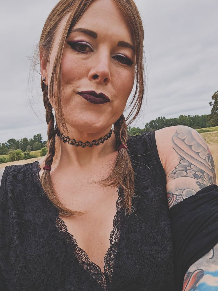 Selfie of jade, outdoors, wearing a black lacey top. Her hair is in braids and makeup is gothy. 