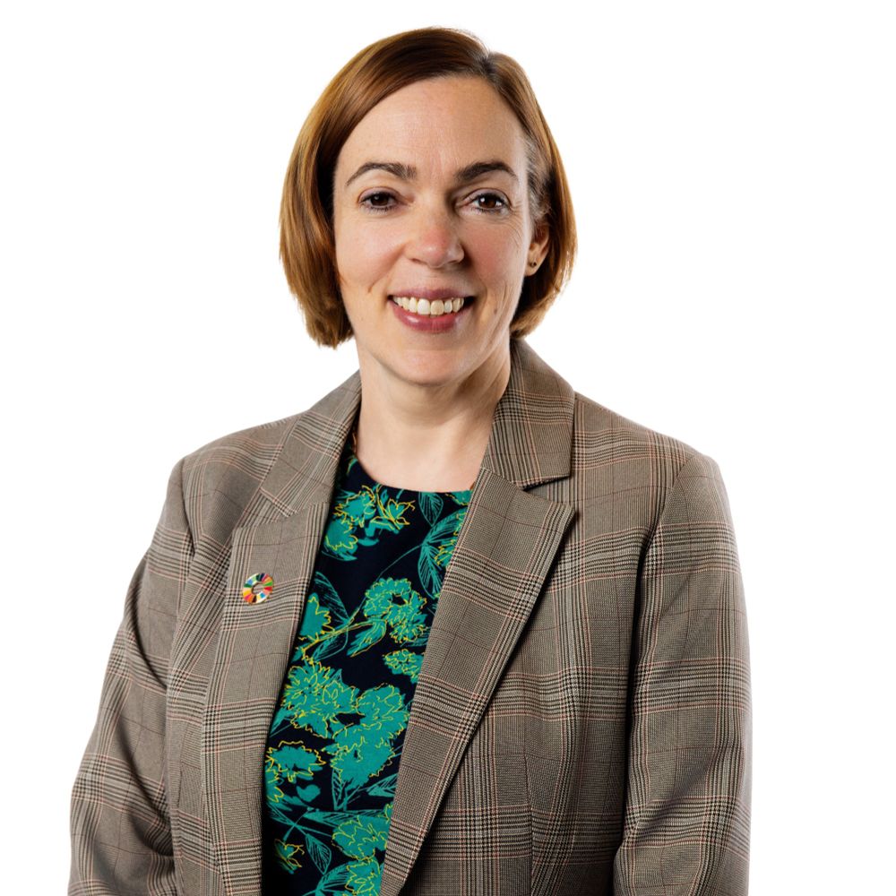 Professor Sarah Sharples smiles, wearing a brown blazer and black and green dress