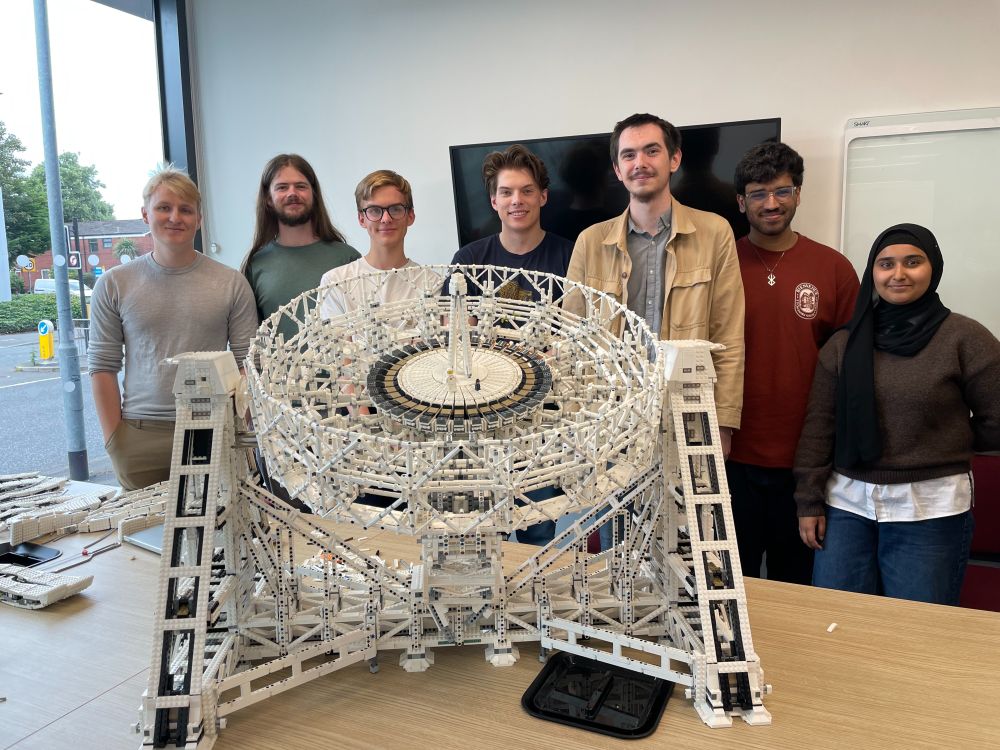 Seven Physics students stand behind a LEGO model of the Lovell Telescope smiling