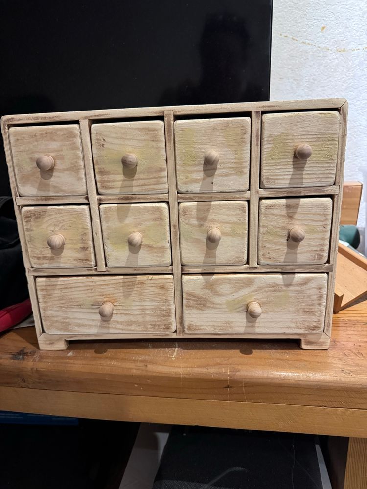 A spice chest style box with drawers that has had its finish sanded off, and all its sharp edges worn down. In the center of each drawer is a fixed a small round wooden knob.