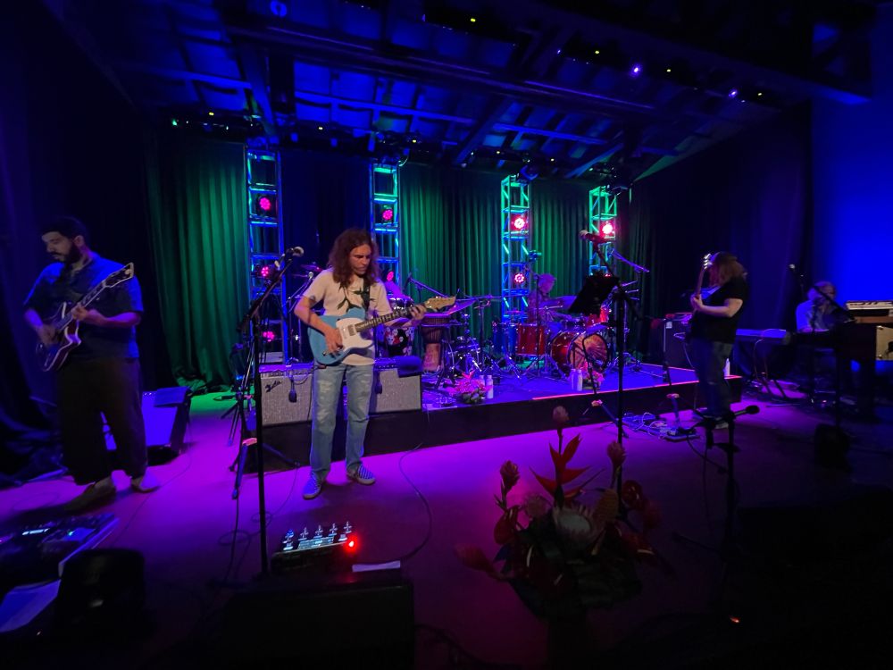 Mahalo Dead band playing on a stage dimly lit with blue, purple and green. 