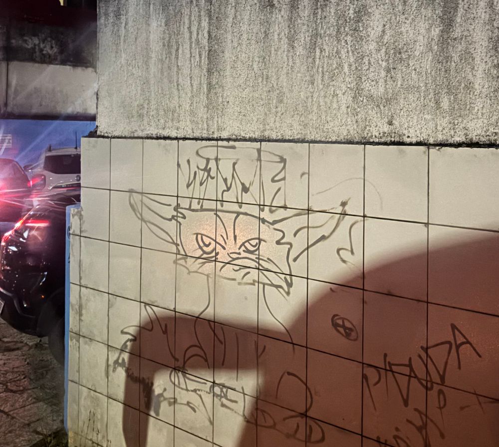 Pichação em um muro revestido com azulejos brancos em forma de um gato com cara enfezada e uma auréola de anjo sobre a cabeça dele