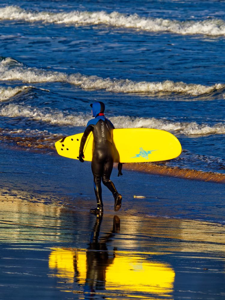 Picture of a surfer carrying a yellow board at the water's edge with a reflection of the surfer in the foreground in wet sand.

Olympus E-M1MarkII
LEICA DG 100-400/F4.0-6.3 lens 
@ƒ/5.6 224.0mm 1/800s ISO200
